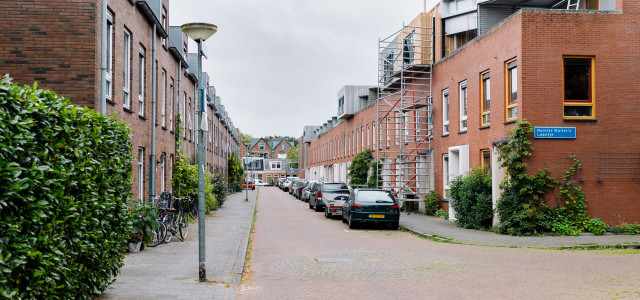Een straat in de wijk Oosterpoort in Groningen. De huizen rechts hebben rode/oranje bakstenen. Er is een steiger voor een van de huizen. Op straat zijn auto's geparkeerd. De huizen links hebben bruine bakstenen.