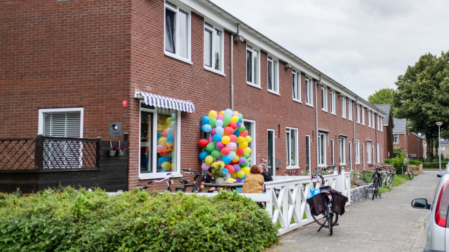Een foto van rijtjeshuizen in Groningen. Er staat een fiets op de stoep geparkeerd. Rechtsvoor zie je wat auto's. Om de voordeur van het hoekhuis hangen allemaal ballonnen.