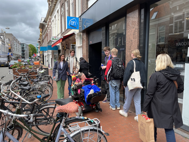 Foto is gemaakt voor de Albert Heijn, hier is Anneke te zien in haar rolstoel en ze kan er amper langs door de fietsen en voetgangers.