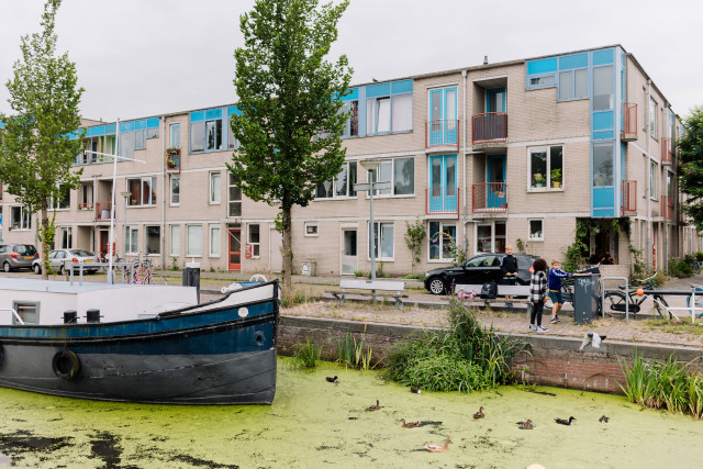 Een foto van een wijk in Groningen met op de voorgrond een woonboot de kade waar kinderen op spelen met op de achtergrond een rij woningen