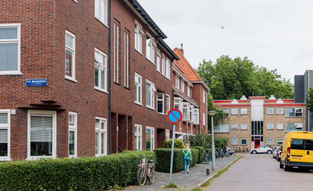 Foto van het Van Brakelplein in Groningen. Je ziet een straathoek met naambordje. Er loopt iemand met blond haar op de stoep. Link vooraan staat een grote gele bus.