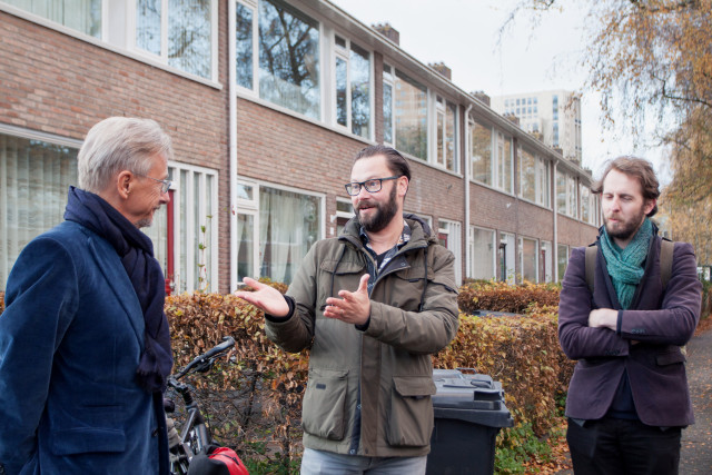 Foto: Drie mannen buiten voor een rij huizen staan met elkaar te praten 